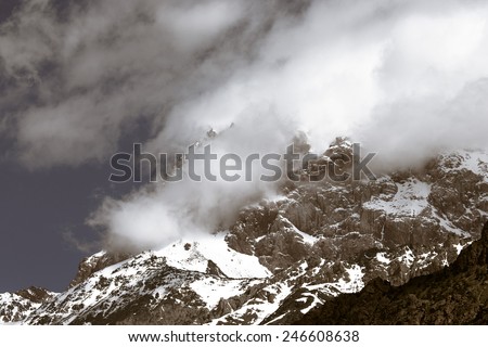 Clouds lie on the snow-covered tops of the rocks. Landscape. Toned.