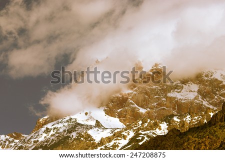 Clouds lie on the snow-covered tops of the rocks. Landscape. Toned.