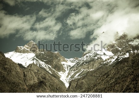 Clouds over the snow-covered tops of the rocks. Landscape. Toned.