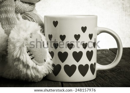 Paw of Teddy bear  and mug with hearts on the old wooden table. Toned.
