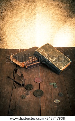 Vintage books and coins and spectacles on old wooden table. Toned