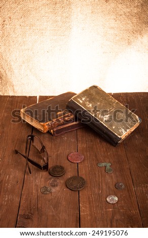 Vintage books and coins and spectacles on old wooden table. Toned