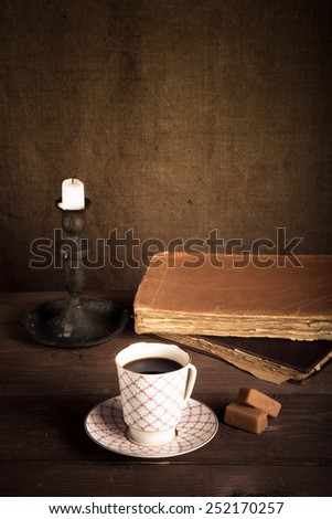 Stack of old books, cup of coffee, candy and candle on the old wooden table. Toned.