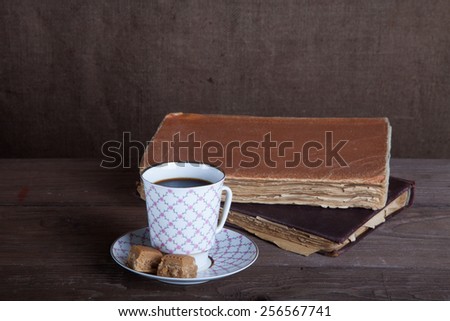 Old books and a cup of coffee with two candies on an old wooden table.