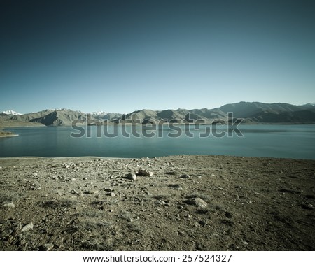 Beautiful landscape - clear mountain lake in rocky valley. The rocky mountains and blue sky are behind. Toned.