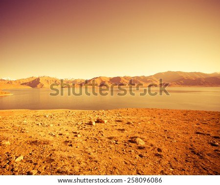 Beautiful landscape - clear mountain lake in rocky valley. The rocky mountains and blue sky are behind. Toned orange.