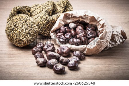 Chestnuts in a paper bag and knitted hat on a light wooden table. Toned.