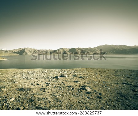 Beautiful landscape - clear mountain lake in rocky valley. The rocky mountains and blue sky are behind. Toned gray.