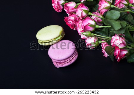 Roses with a lot of leaves and macaroons on a black background. Space for text.