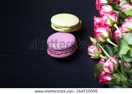 Roses with a lot of leaves and macaroons on a black background. Space for text. Toned.