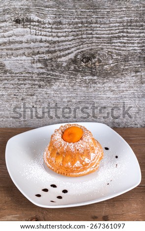 Cake with dry apricot and sugar powder on the white plate on wooden table. Selective focus.