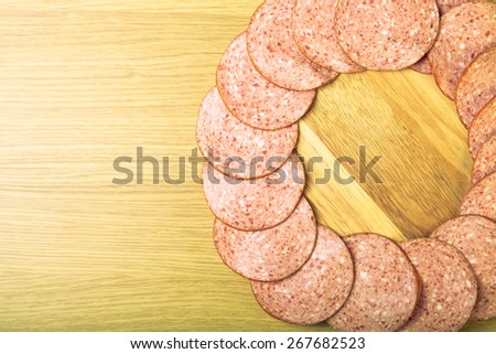 Few slices of sausage lies in the shape of ring on a light wooden table. Toned.