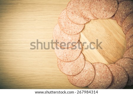 Few slices of sausage lies in the shape of ring on a light wooden table. Toned.