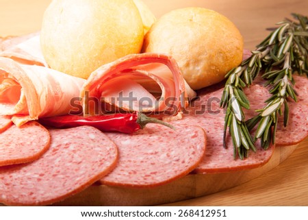 Slices of sausage and bacon on a cutting board with bread rolls, chilli pepper and rosemary. Toned.