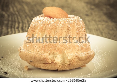 Cake with dry apricot and sugar powder on the white plate on wooden table.Toned.  Selective focus.