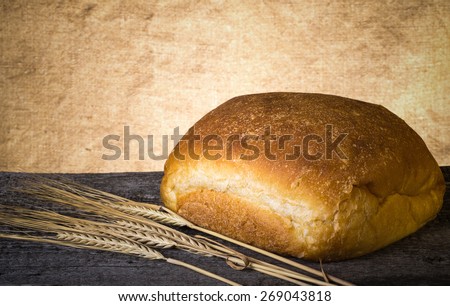 Loaf of white wheat bread and wheat ears on an old wooden table. Toned.