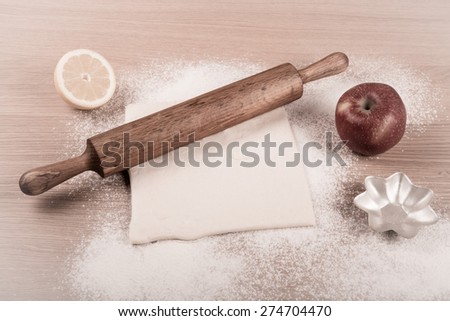 Dough, rolling pin, forms for baking, apple, half of lemon and flour sprinkled on a light wooden table. Toned.