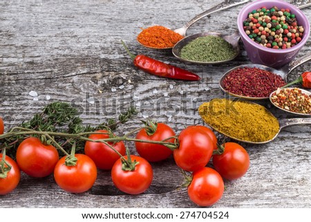 Bunch of cherry tomatoes, herbs, small bowl and antic metal spoons with different kinds of spices, sea salt and red hot chili peppers on old wooden board. Selective focus.