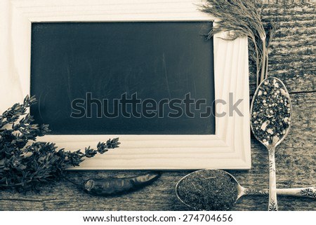 Herbs, chili, antique metal spoons with spices and black chalk board in a light wooden frame on the old wooden table. Toned.