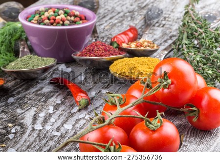 Bunch of cherry tomatoes, herbs, small bowl and antic metal spoons with different kinds of spices, sea salt and red hot chili peppers on old wooden board. Selective focus.