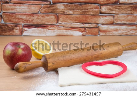 Set for home baking on a light wooden table with flour. Rolling pin, baking form, dough, half of lemon, apple.