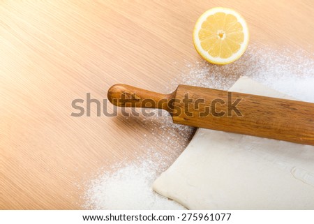Dough, rolling pin, half of lemon and flour sprinkled on a light wooden table. Toned.