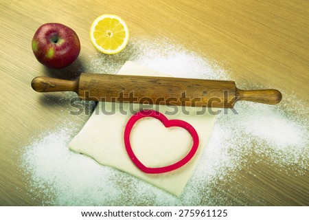 Set for home baking on a light wooden table with flour. Rolling pin, baking form, dough, half of lemon, apple. Toned.