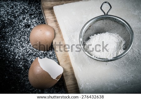 Set for home baking on a black background with flour. Dough, board, eggshell and flour. Toned