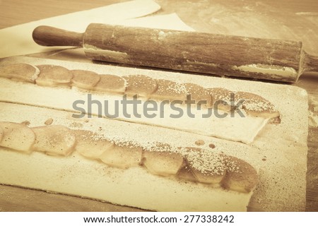 Apple slices on stripes of dough and rolling pin on a light wooden table with flour. Toned.