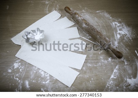 Stripes of dough, rolling pin and baking form on a light wooden table with flour. Toned.