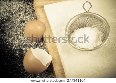 Set for home baking on a black background with flour. Dough, board, eggshell and flour. Toned