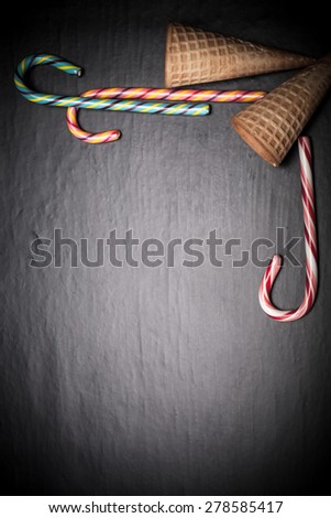 Candy sticks and waffle cones for ice cream on a black background. Space for text. Toned.