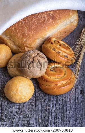 Different types of fresh bread and wheat ears on old wooden table. Toned.