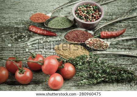 Bunch of cherry tomatoes, herbs, small bowl and antic metal spoons with different kinds of spices, sea salt and red hot chili peppers on old wooden board. Selective focus. Toned.