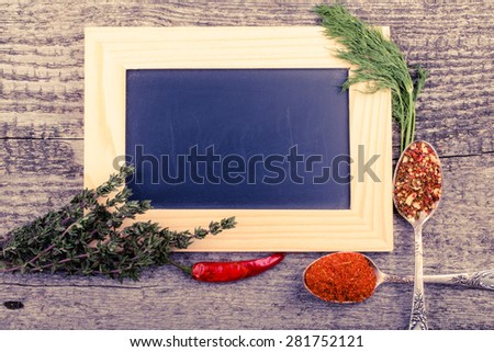 Herbs, chili, antique metal spoons with spices and black chalk board in a light wooden frame on the old wooden table. Toned.