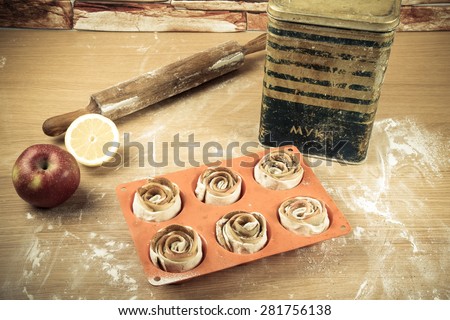 Silicone form with homemade pastries, a rolling pin, a jar of flour, half a lemon and an apple on a light wooden table. Toned.