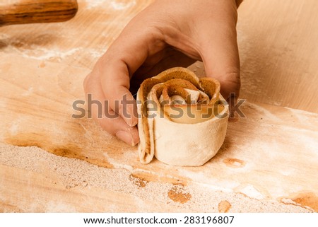 Female hand twists the apple slices in the dough strip on a light wooden table with flour. Toned.