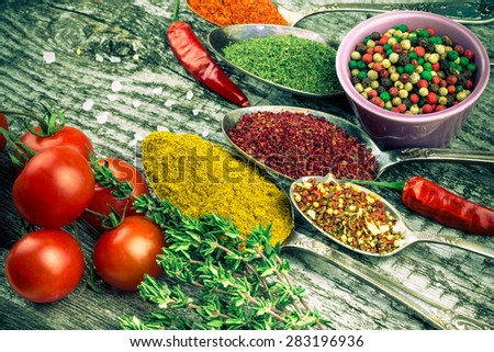 Bunch of cherry tomatoes, herbs, small bowl and antic metal spoons with different kinds of spices, sea salt and red hot chili peppers on old wooden board. Selective focus. Toned.