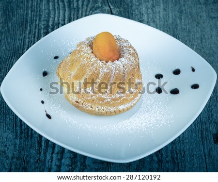 Cake with dry apricot and sugar powder on the white plate on wooden table. Selective focus. Toned.