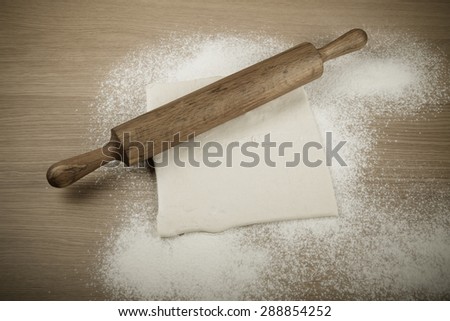Rolling pin, dough and baking form on a light wooden table with flour. Toned.