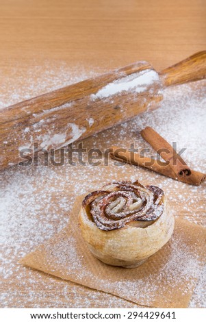 Homemade pastries with cinnamon on a light wooden table with flour.