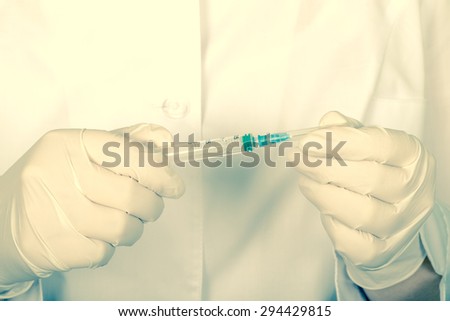 Doctor holds in hands a syringe with a needle closed. Close-up. In the hands wearing surgical gloves. Tinted.