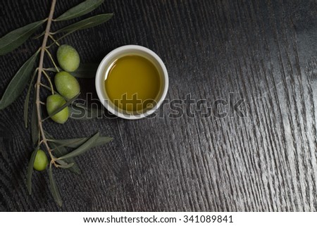 Branch of olive tree with green olive berries and cap of fresh olive oil on a black wooden table or board.