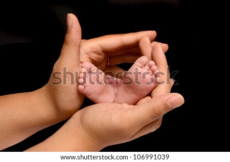 A loving and caring mother is holding the feet of her first new born baby girl and gently enclosing her soft and warm fingers and palms around the tiny little girls feet and toes