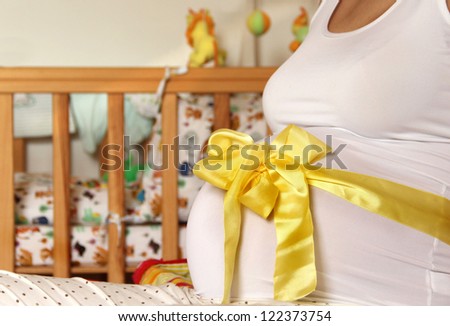 Pregnant woman tummy decorated with yellow ribbon and bow