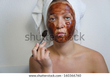 Young beautiful woman applying chocolate mask on her face
