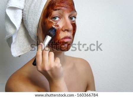 Young beautiful woman applying chocolate mask on her face