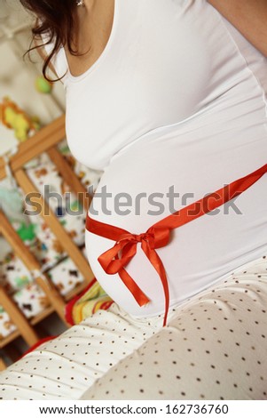 Pregnant woman tummy decorated with red ribbon and bow