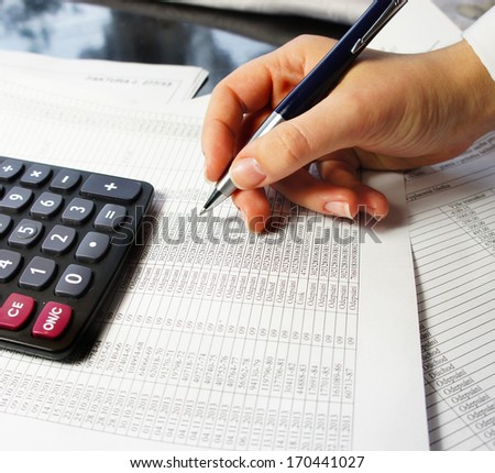Calculator, pen and accounting document with a lot of numbers and woman\'s hand.