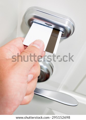 A person\'s hand sliding a card key into an electronic door lock security system on a hotel room